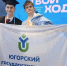 На фотографии два молодых человека держат флаг Югорского государственного университета. На флаге изображен логотип университета, а также надпись - ЮГУ